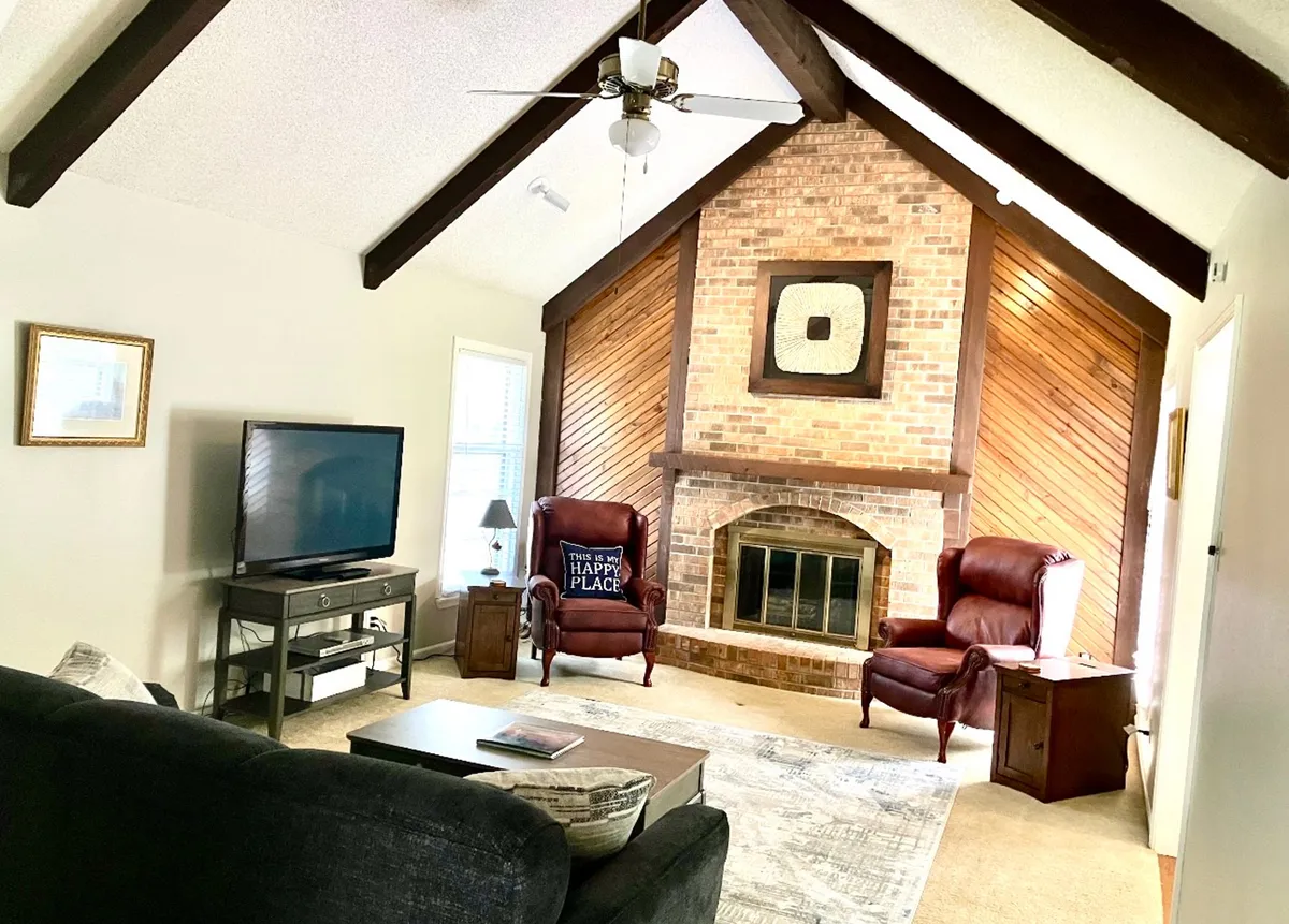 A warm living area featuring a brick fireplace flanked by reclining chairs and a coffee table, with a TV positioned for easy viewing. The inviting seating arrangement encourages relaxation and togetherness, ideal for families to unwind after hospital visits or busy days.