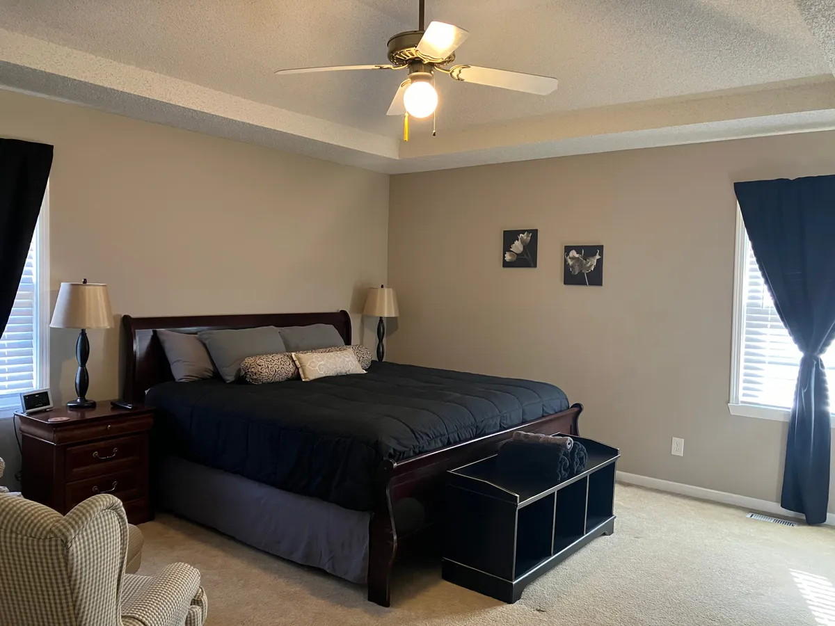 A cozy bedroom featuring a comfortable bed flanked by nightstands, a window letting in soft natural light, a chair for quiet reading, and tasteful wall art. The space exudes warmth and privacy, perfect for restful sleep or a peaceful retreat.