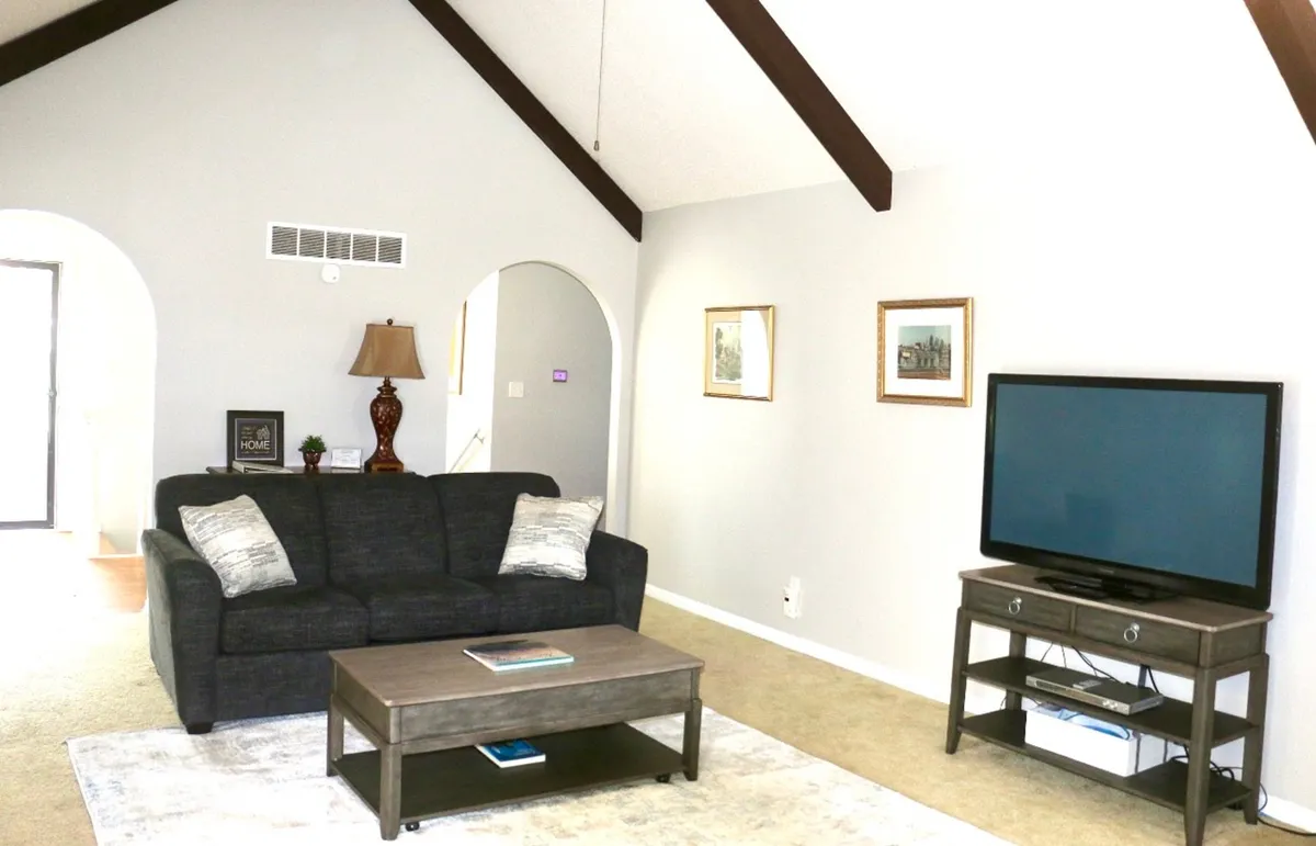 A comfortable lounge area with a soft sofa, coffee table, television, warm lamp, and tasteful artwork. The space is bathed in natural light and arranged to encourage lounging, socializing, or quiet contemplation, perfectly matching the section’s emphasis on peaceful mornings, birdwatching, and cozy relaxation.
