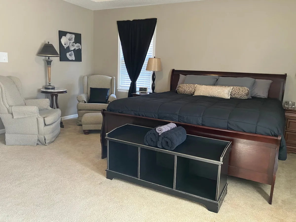 A tranquil bedroom space featuring a comfortable bed adorned with decorative pillows, a reading chair, soft lighting from a table lamp, and carefully selected wall art. The atmosphere is intimate and relaxing, perfect for unwinding in privacy.