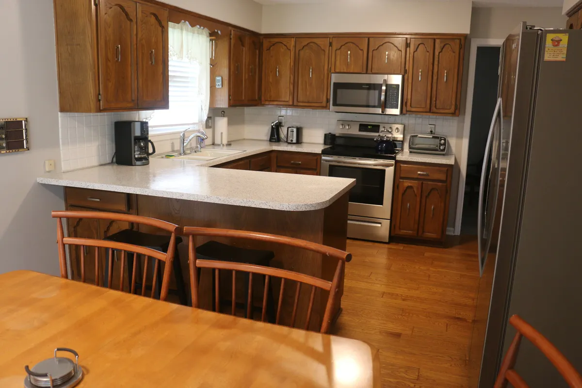 This image provides a wide-angle view of the kitchen and dining area, showcasing the kitchen island, stainless steel appliances, wooden cabinets, and a dining table. The layout emphasizes an open, communal space perfect for cooking, gathering, and sharing meals.