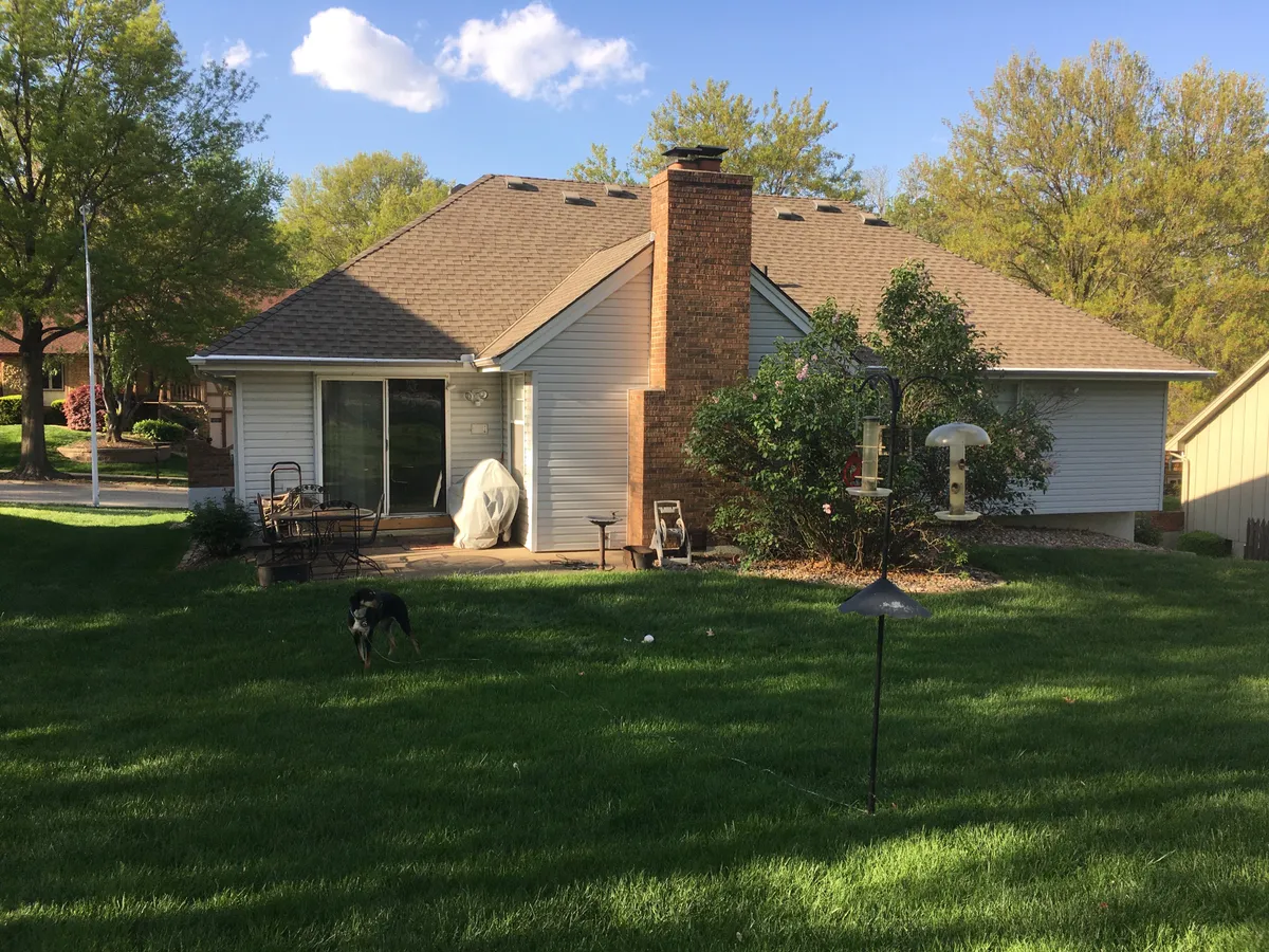 This exterior photo features a lush green lawn, a charming brick chimney, inviting patio furniture, and a bird feeder set in a tranquil backyard. The scene suggests a relaxing natural setting perfect for enjoying the outdoors. The bird feeder is front and center, highlighting opportunities for birdwatching right outside the home.