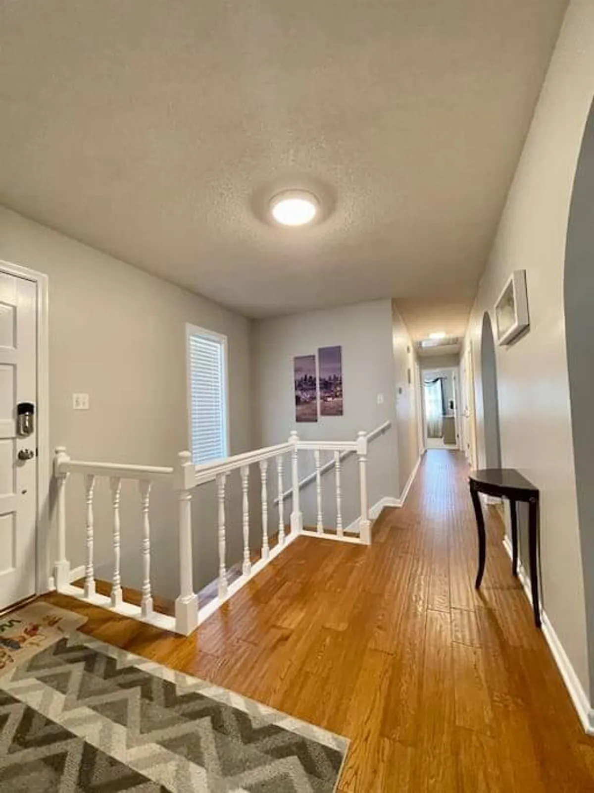 A well-lit transitional space with a prominent staircase railing, stylish decorative rug, and wall art sets the tone for the home's playful decor. The area feels inviting, hinting at the whimsical touches and cozy character that continue throughout the living spaces.