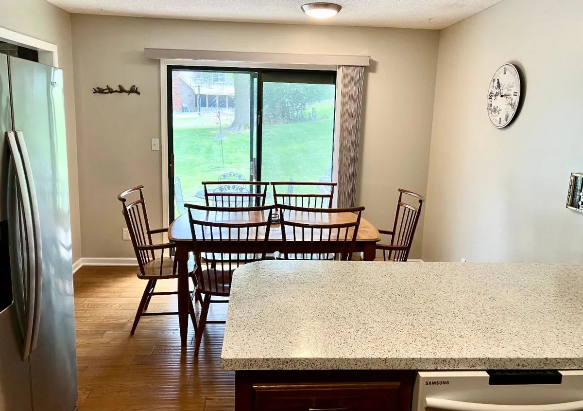 A cozy dining table sits adjacent to a sliding glass door, with the kitchen counter in close proximity. The table is set for gatherings, capturing the warmth of family meals and the inviting nature of the dining area.