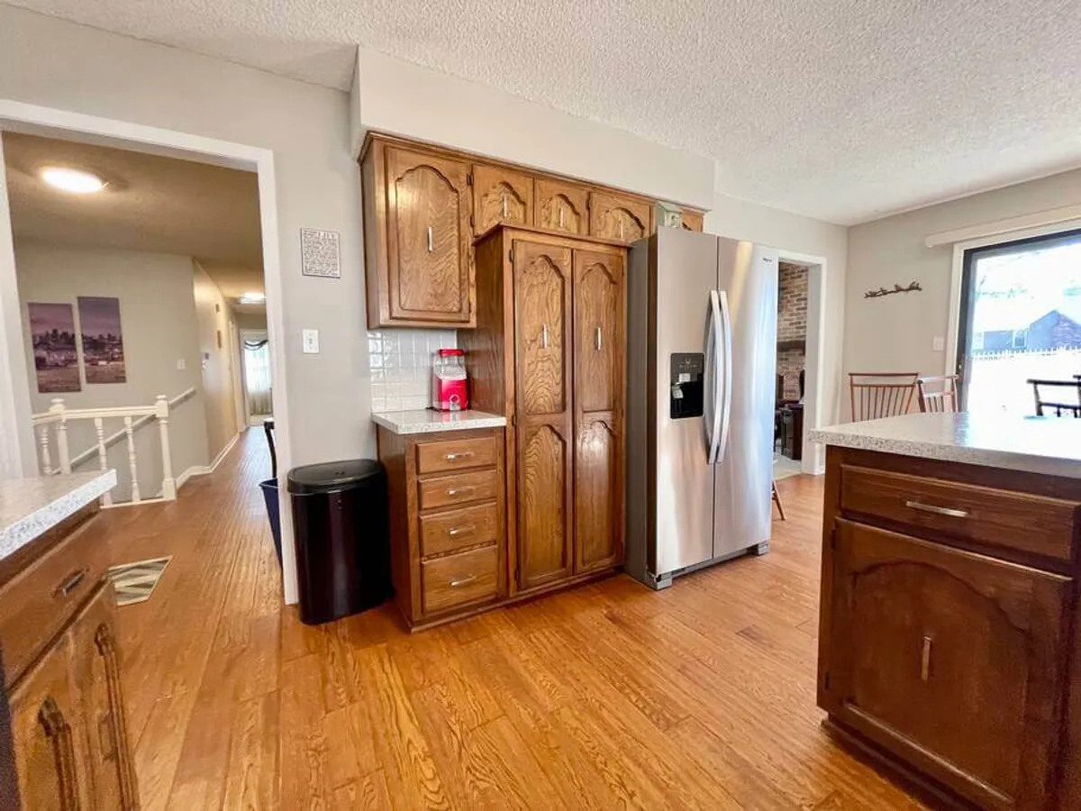A welcoming kitchen with rich wooden cabinetry, stainless steel refrigerator, and wooden flooring. The spacious layout is ideal for family gatherings, meal preparation, or simply enjoying home-cooked food together.